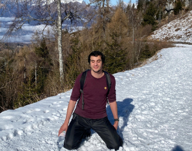 Hasan kneeling in deep snow on a mountain path, smiling, with clear sky and mountains in the background, symbolising his Everest dream