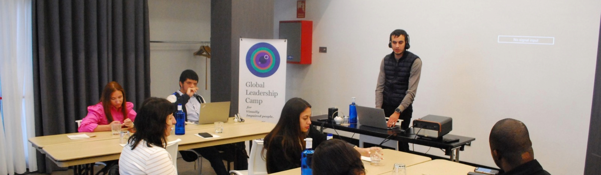 Hasan stands at the front of a professional workshop, leading a session for engaged participants at the Global Leadership Camp